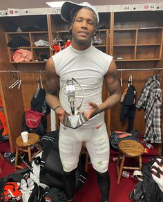 a man standing in a dressing room holding a trophy and looking at the camera while wearing all white