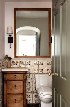 a white toilet sitting next to a wooden cabinet in a bathroom under a large mirror