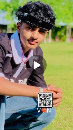 a young man sitting on top of a lush green field wearing a black hat and sunglasses