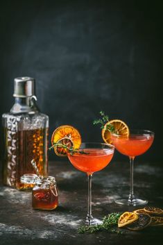 two cocktails with orange garnish sit on a table