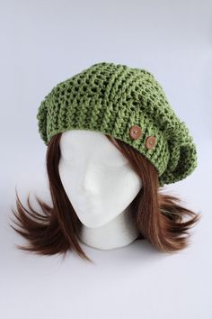 a white mannequin head wearing a green crochet hat with brown buttons