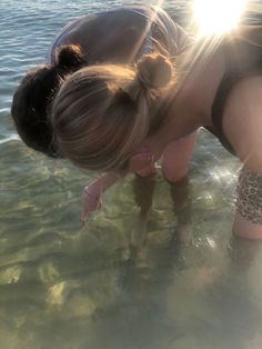 a woman bending over in the water with sun shining on her face and arm behind her