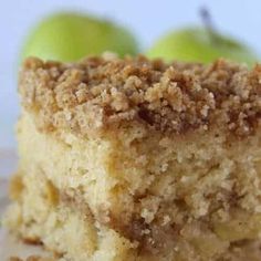 a piece of cake sitting on top of a white plate next to two green apples