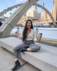 a woman sitting on a concrete bench with her legs crossed and holding a cup in one hand