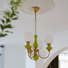 a green chandelier hanging from the ceiling in a room with white walls and curtains