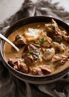 a close up of a bowl of food with meat and mushrooms in it on a table