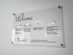 a welcome sign hanging on the wall in front of a white wall with black lettering