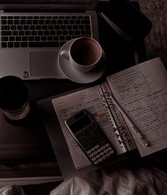 an open book, calculator and cell phone on a desk next to a laptop