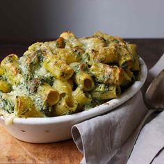 a white bowl filled with pasta on top of a wooden cutting board next to a silver spoon