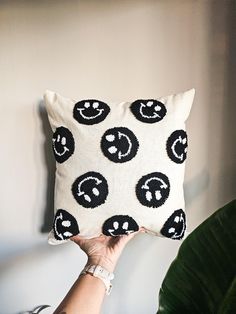 a person holding up a pillow with smiley faces on it in front of a plant