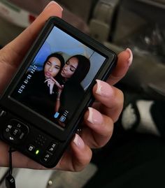 a person holding up a cell phone with two women on it's screen and the other hand