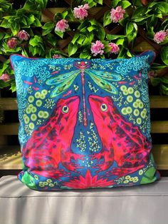 a colorful pillow sitting on top of a wooden bench next to pink and green flowers