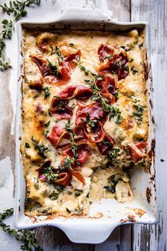 a casserole dish with cheese, bacon and herbs in it on a wooden table