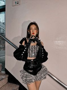 a woman in black jacket and skirt standing on stairs with her hand over her mouth