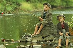 two young boys sitting on rocks in the water fishing