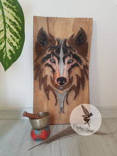 a wooden plaque with a wolf face on it next to a metal bowl and plant