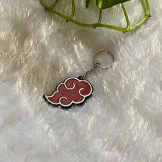 a red and white cloud shaped keychain sitting next to a plant