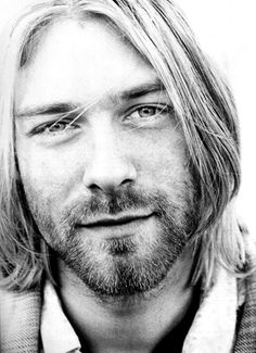 a black and white photo of a man with long hair wearing a sweater looking at the camera