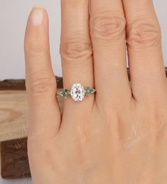 a woman's hand with a diamond and emerald engagement ring