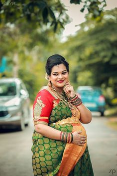 a woman in a green and red sari standing on the side of a road