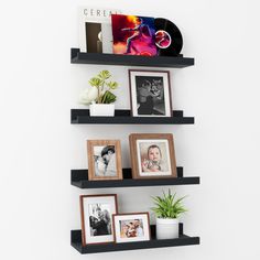 three black shelves with pictures, photos and plants on them against a white wall in the corner