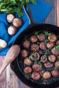 a skillet filled with mushrooms on top of a wooden table next to parsley