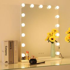 a table with a mirror and some flowers on it next to a box of makeup