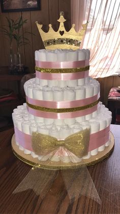 a three tiered cake decorated with diapers and a gold crown on top, sitting on a wooden table