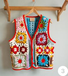 a crocheted vest hanging on a wooden hanger next to a white wall