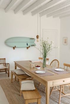 a dining room table and chairs with a surfboard on the wall above it,