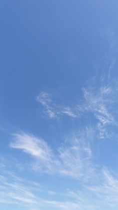 two people standing on the beach flying a kite in the blue sky with white wispy clouds