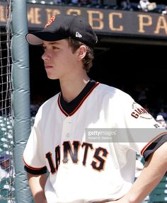 a young baseball player standing in front of the dugout at a ball park, waiting for his turn to bat