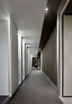 a long hallway with white walls and black flooring is lit by recessed lighting