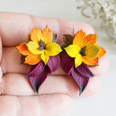 a person is holding two fake leaves in their hand, one has yellow and red flowers on it