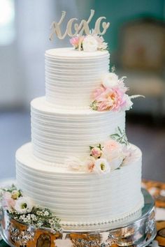 a white wedding cake with pink flowers and the word roxg on top is sitting on a table