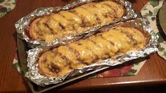 two hot dogs covered in cheese sitting on top of tin foil next to a plate