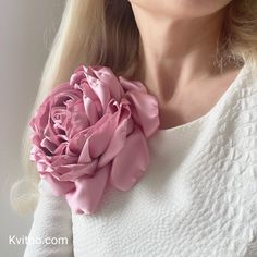 a woman wearing a pink flower on her neck and white sweater with long blonde hair