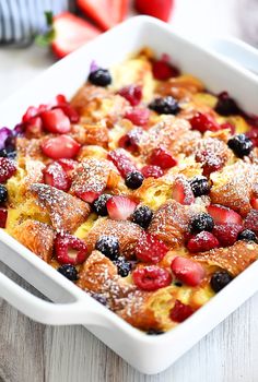 a casserole dish with berries and powdered sugar on top, sitting on a wooden table