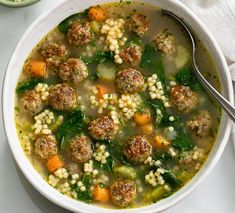 a white bowl filled with meatball soup next to a spoon and some rice on the side