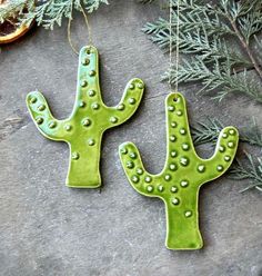 two green cactus shaped magnets sitting on top of a stone floor next to a plant