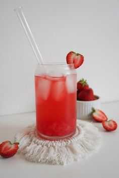 a drink with strawberries and ice on a white table next to some strawberries