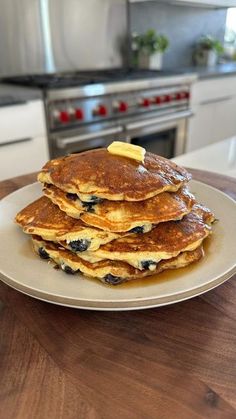 stack of pancakes with butter and blueberries on a plate in front of an oven