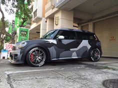 a grey and black camouflage minivan parked in front of a building