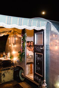 two women are sitting in the back of a food truck with lights on it's sides