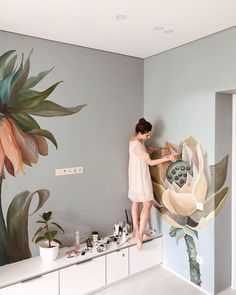 a woman is painting a mural on the wall in her living room with flowers and plants