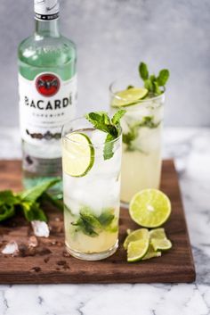 two glasses filled with lemonade and mint on a cutting board next to a bottle of bacardi