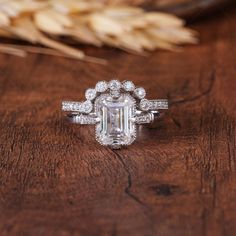 an emerald cut diamond ring on top of a wooden table with wheat stalks in the background