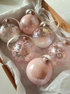 six pink glass ornaments in a box on top of white tissue paper with ribbon around them