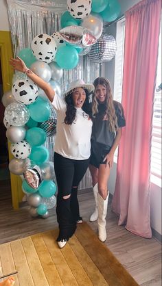 two women standing next to each other in front of balloons