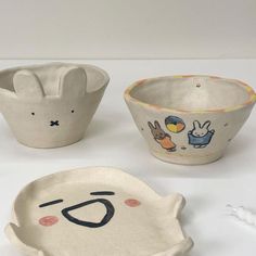 three ceramic bowls with faces on them, one has an animal face and the other has a rabbit's head